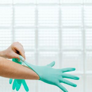 Close-up of a healthcare professional wearing teal gloves against a bright background.